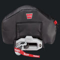 A black carbon-fiber-patterned Winex Warn winch cover with a red and white Warn logo, shown over a silver and black Winex winch with a red warning strap.