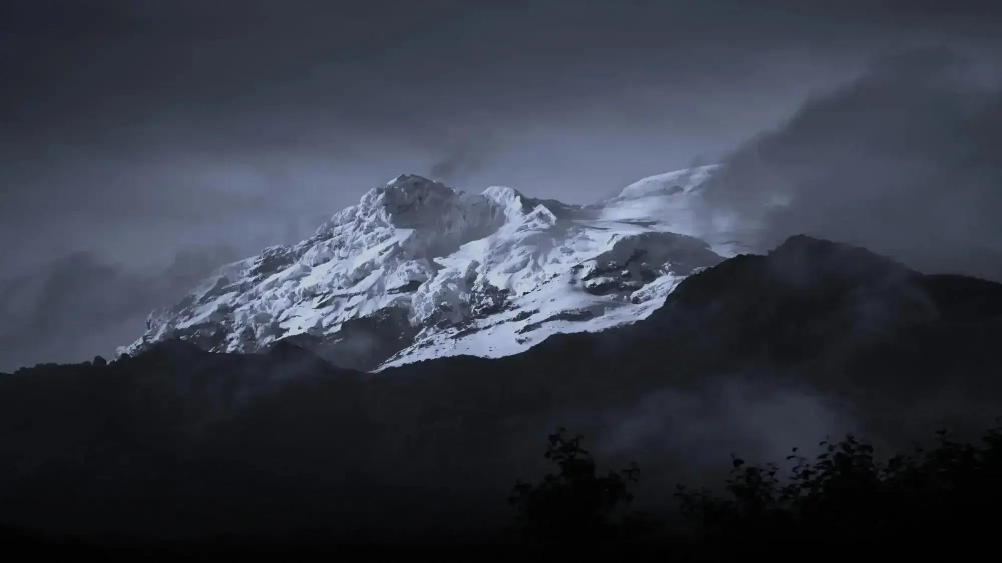 Snowy mountain peak shrouded in mist under a dark sky